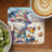 Gnome in floral hat and shorts holding beer mug with pretzels and ice.