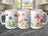 Three white mugs with floral watercolor designs displayed on a dark marble countertop.