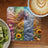 Fantasy art depicting seasons with butterflies, flowers, and woman with latte and kiwi.