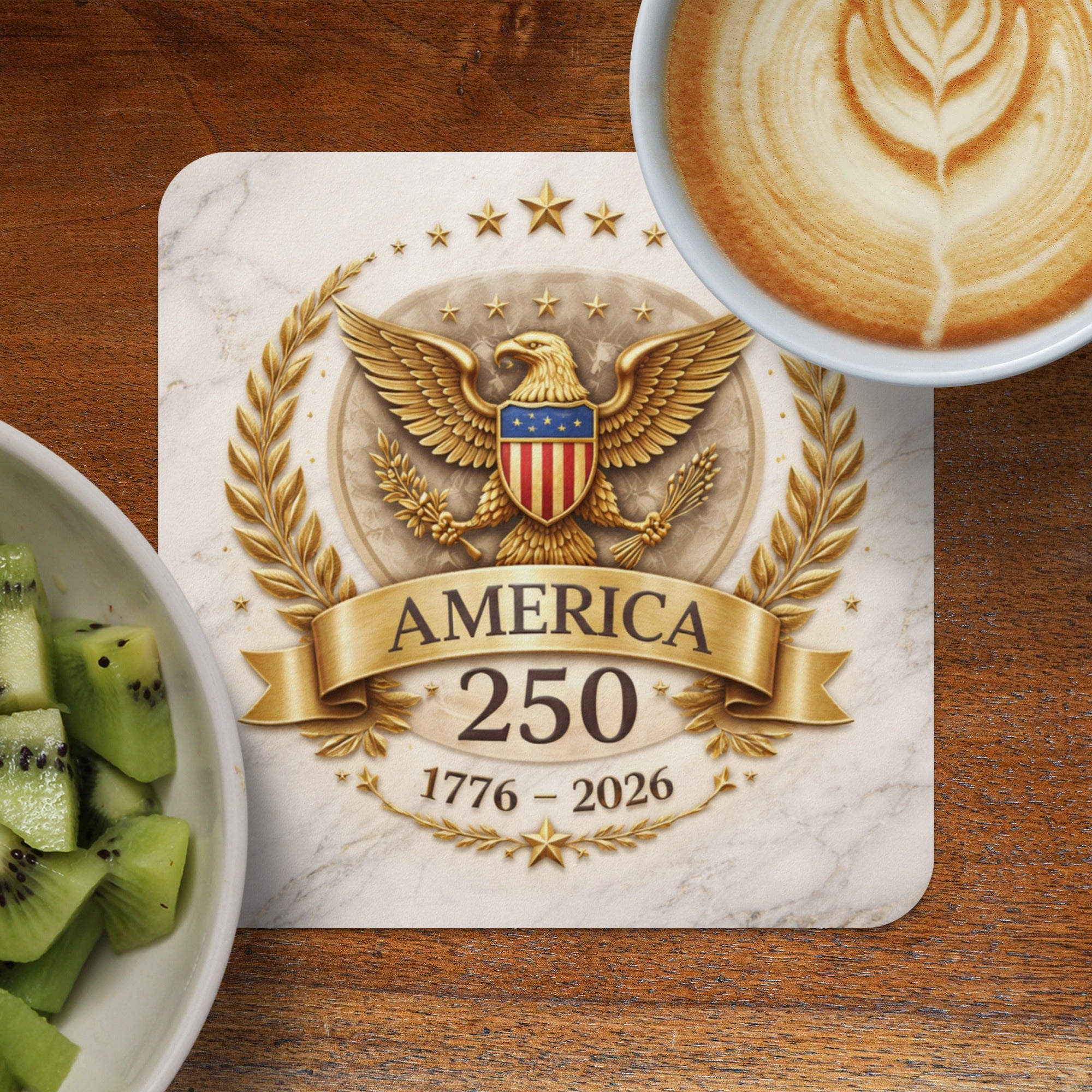 Golden eagle crest with "AMERICA 1776 - 2026" text on marble coaster, coffee, and kiwi.