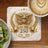 Golden eagle crest with "AMERICA 1776 - 2026" text on marble coaster, coffee, and kiwi.