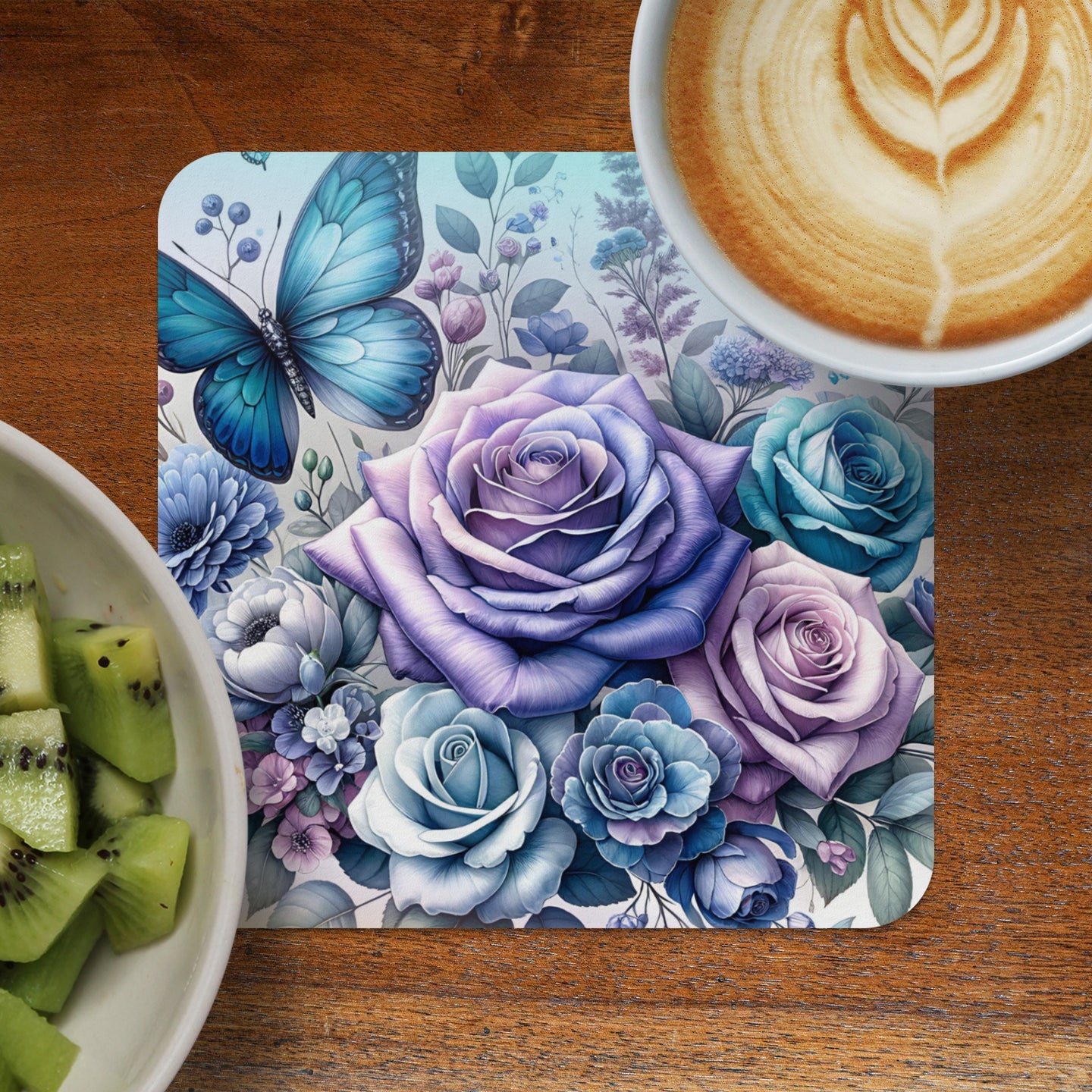 Blue butterfly and purple roses on a floral coaster next to kiwi slices and coffee.