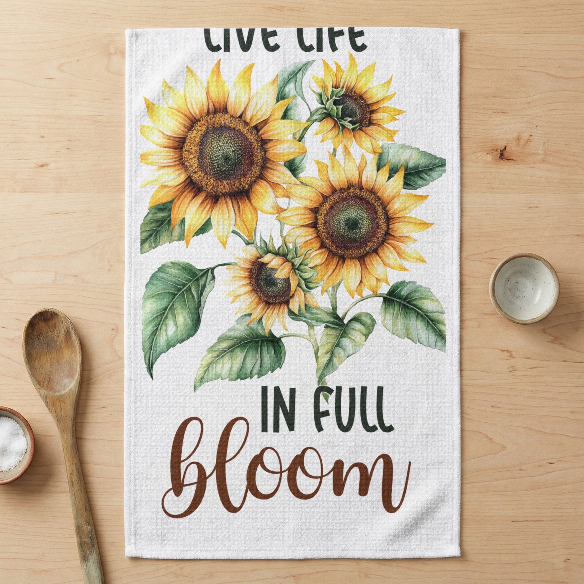 Towels with sunflowers and text "LIVE LIFE IN FULL bloom" on a wooden table.