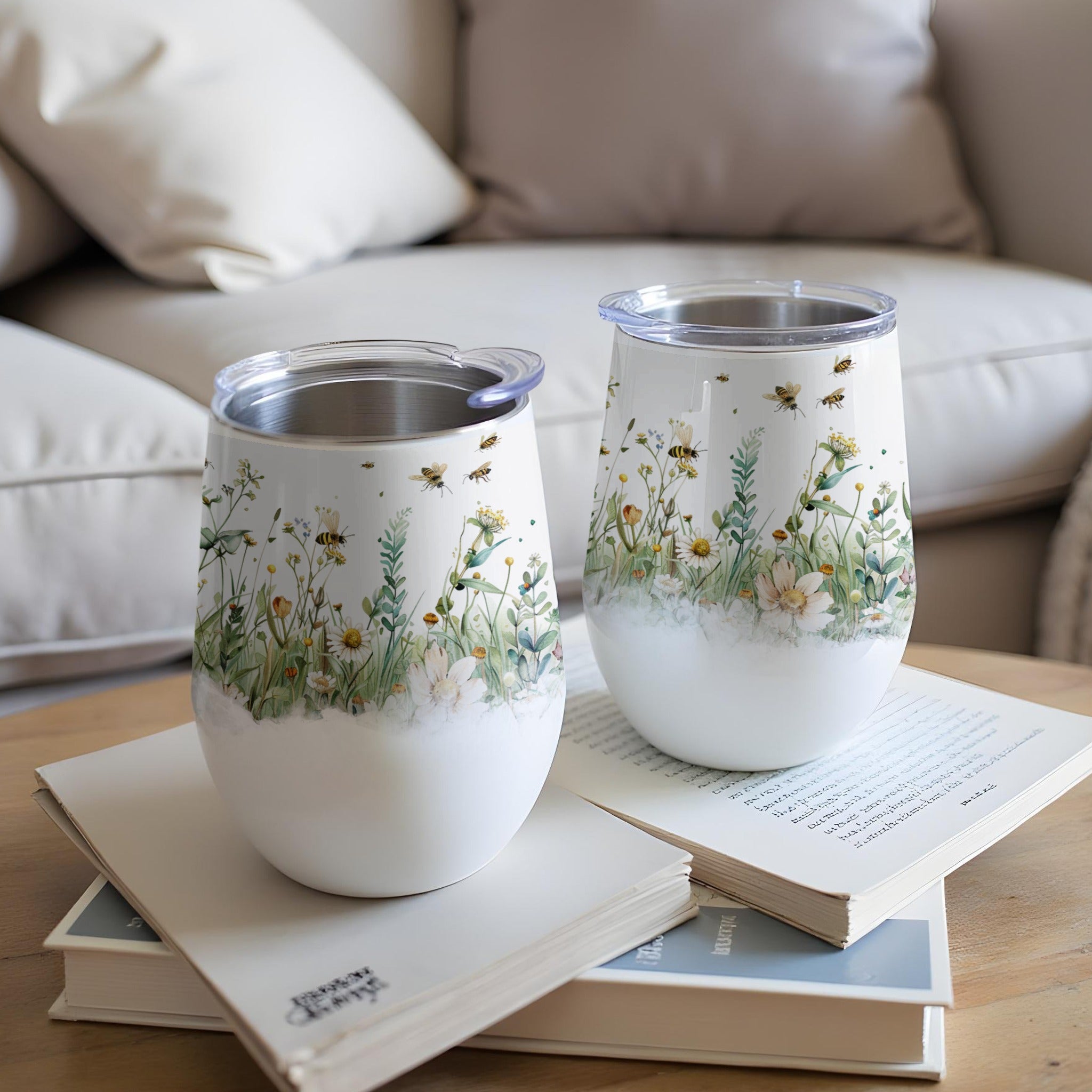 Two tumblers with a floral and bee design sit on books.