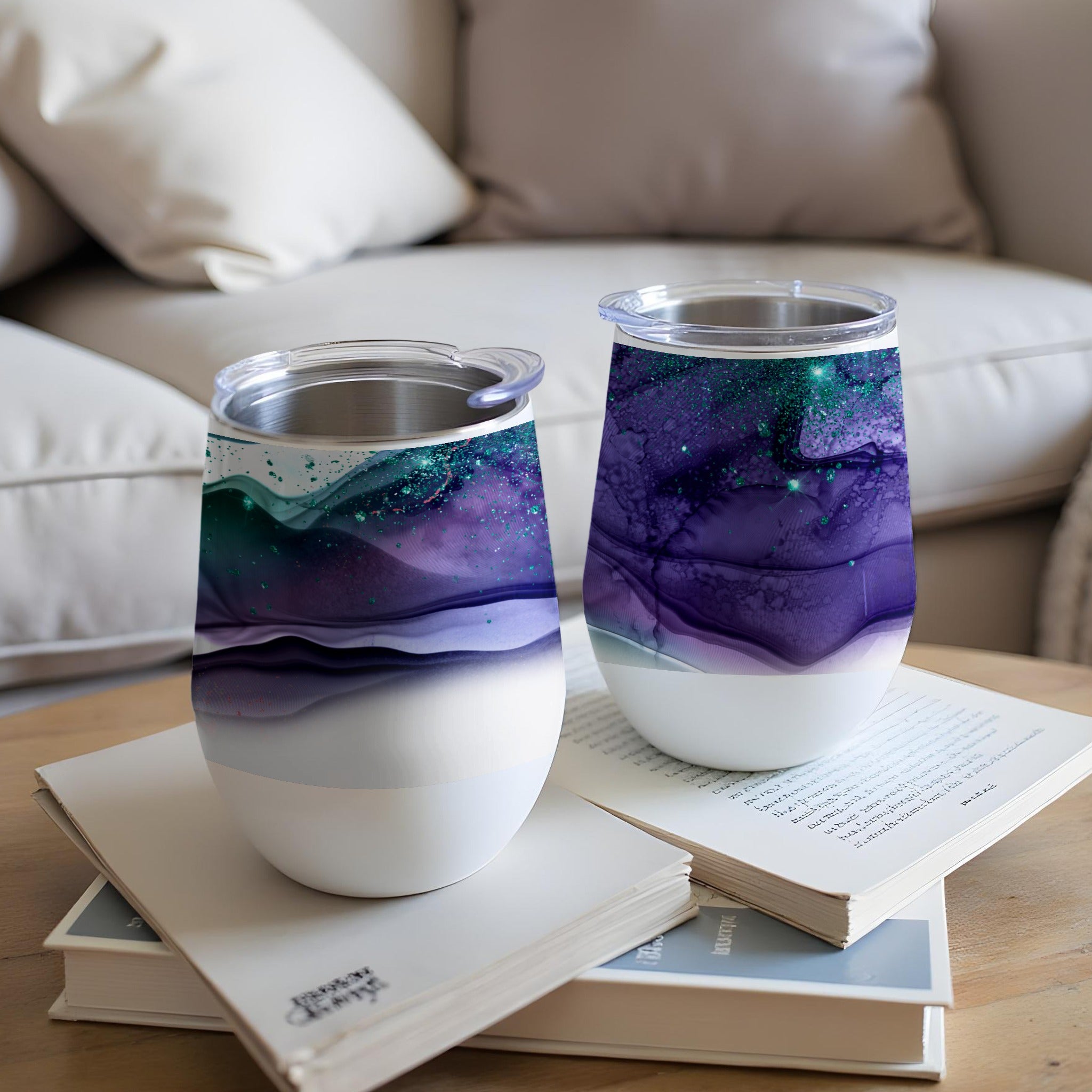 Two tumblers with abstract purple and teal swirl designs sit on books.