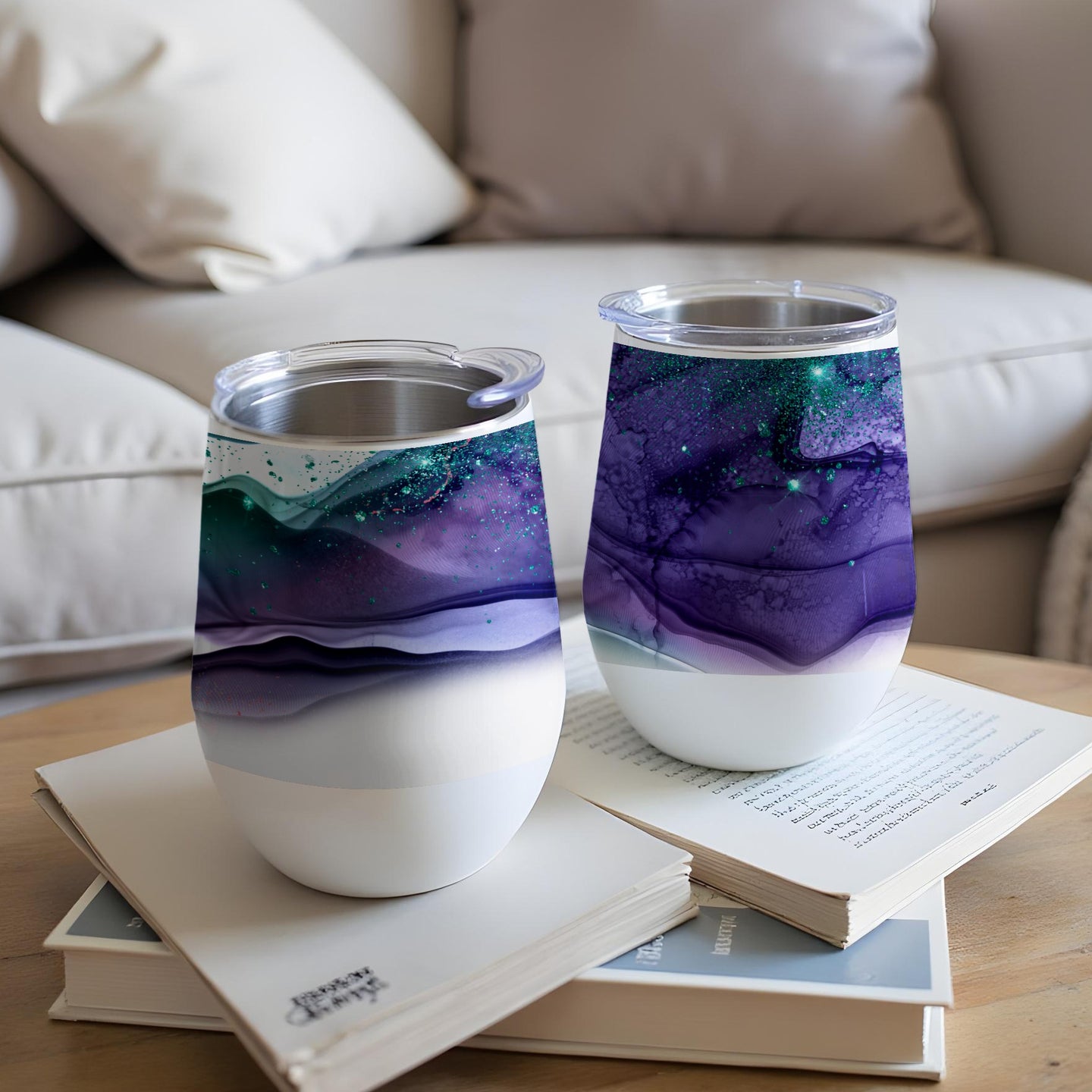 Two tumblers with abstract purple and teal swirl designs sit on books.