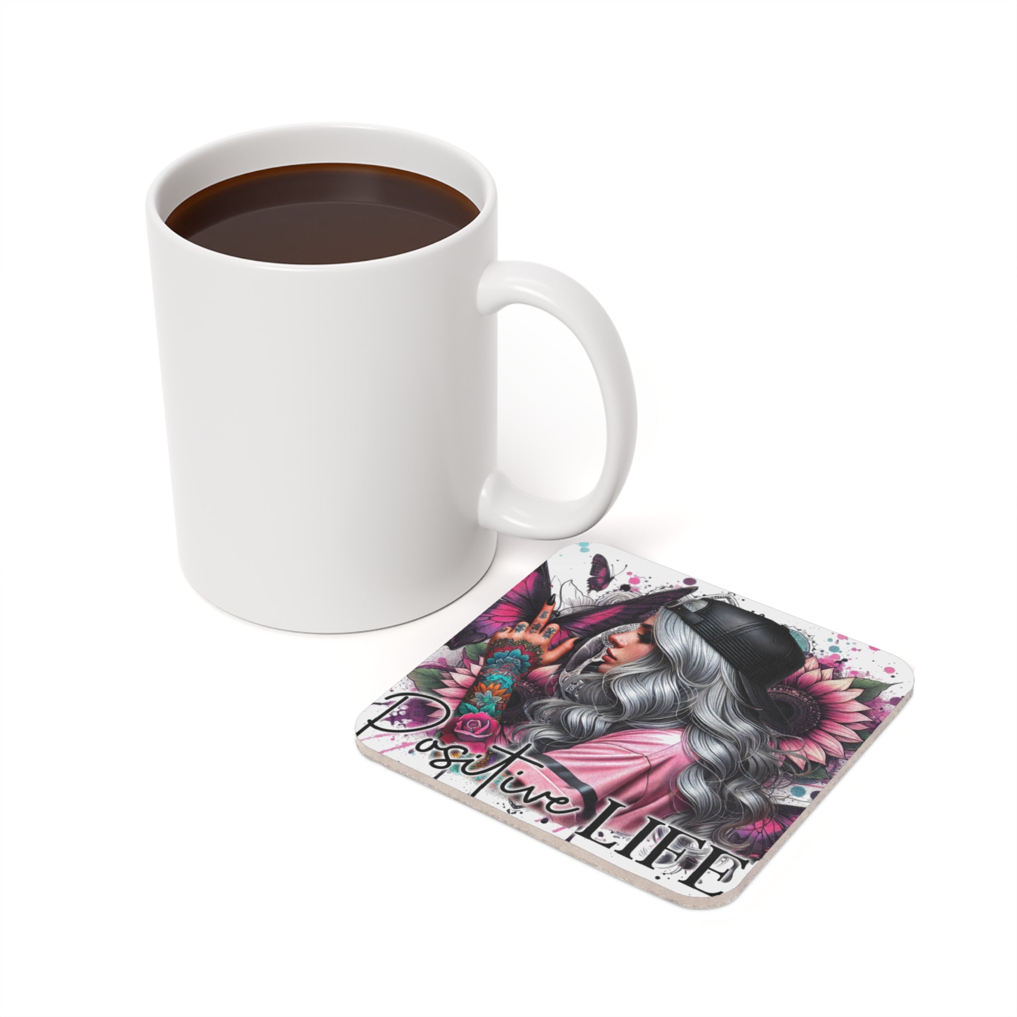 White mug of coffee beside a coaster with "Positive Life" text and colorful designs.