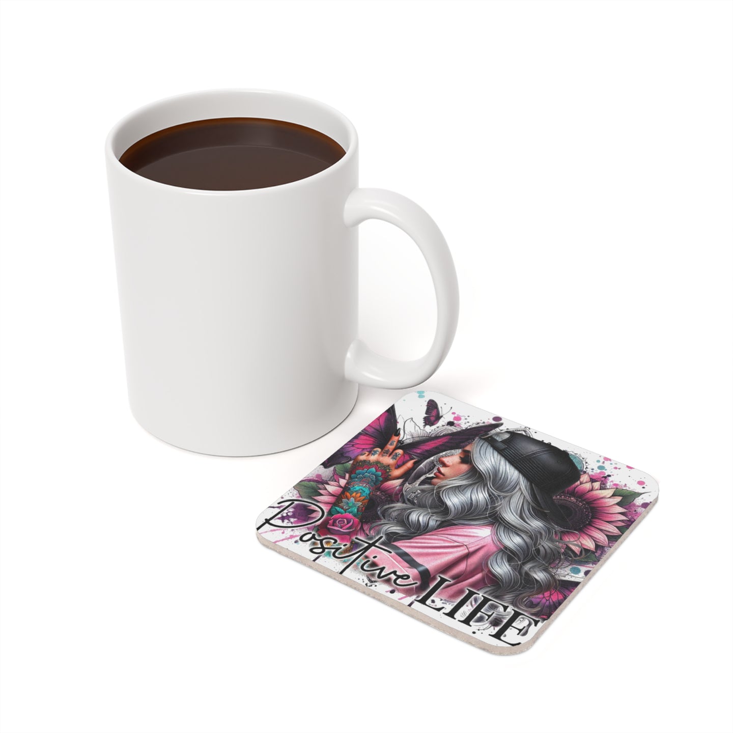 White mug of coffee beside a coaster with "Positive Life" text and colorful designs.