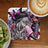 Pink t-shirt and butterfly art on coaster with latte and kiwi.