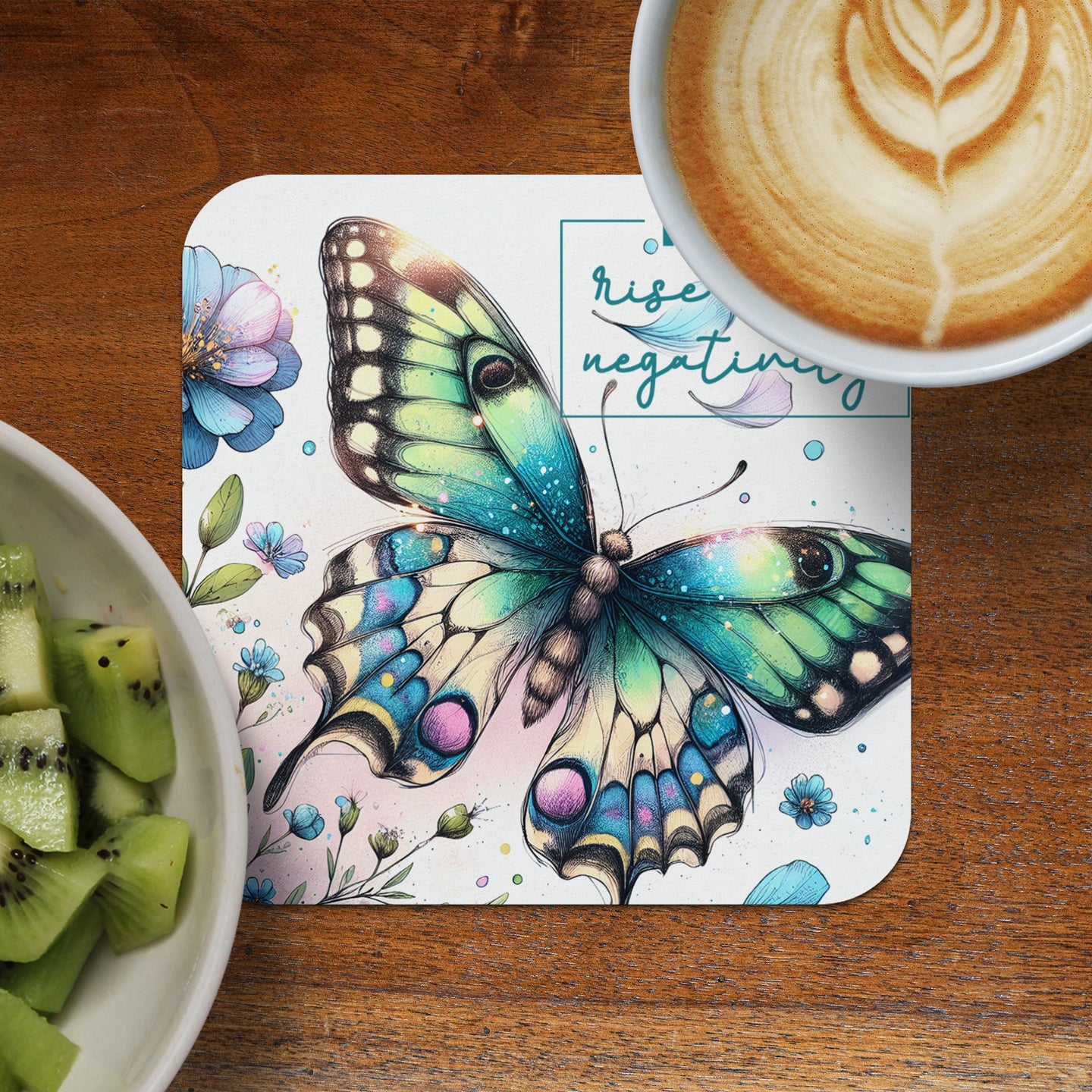 Butterfly art coaster with "Rise negativity" text, next to coffee and kiwi.