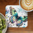 Butterfly art coaster with "Rise negativity" text, next to coffee and kiwi.