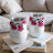 Two white tumblers with pink floral designs sit on books.