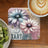 Coaster with two watercolor flowers and text "Just Tart" next to kiwi slices and coffee.