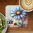 Coaster with blue daisy, ladybug, and text "Just Tart" next to a coffee and kiwi slices.