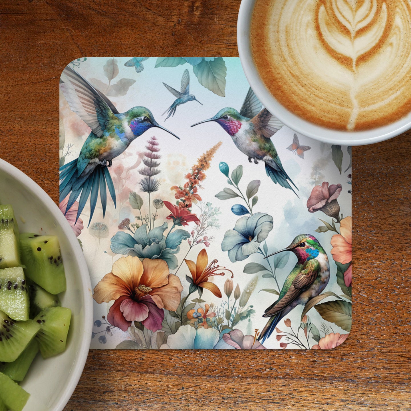 Floral coaster with hummingbirds beside coffee and kiwi.