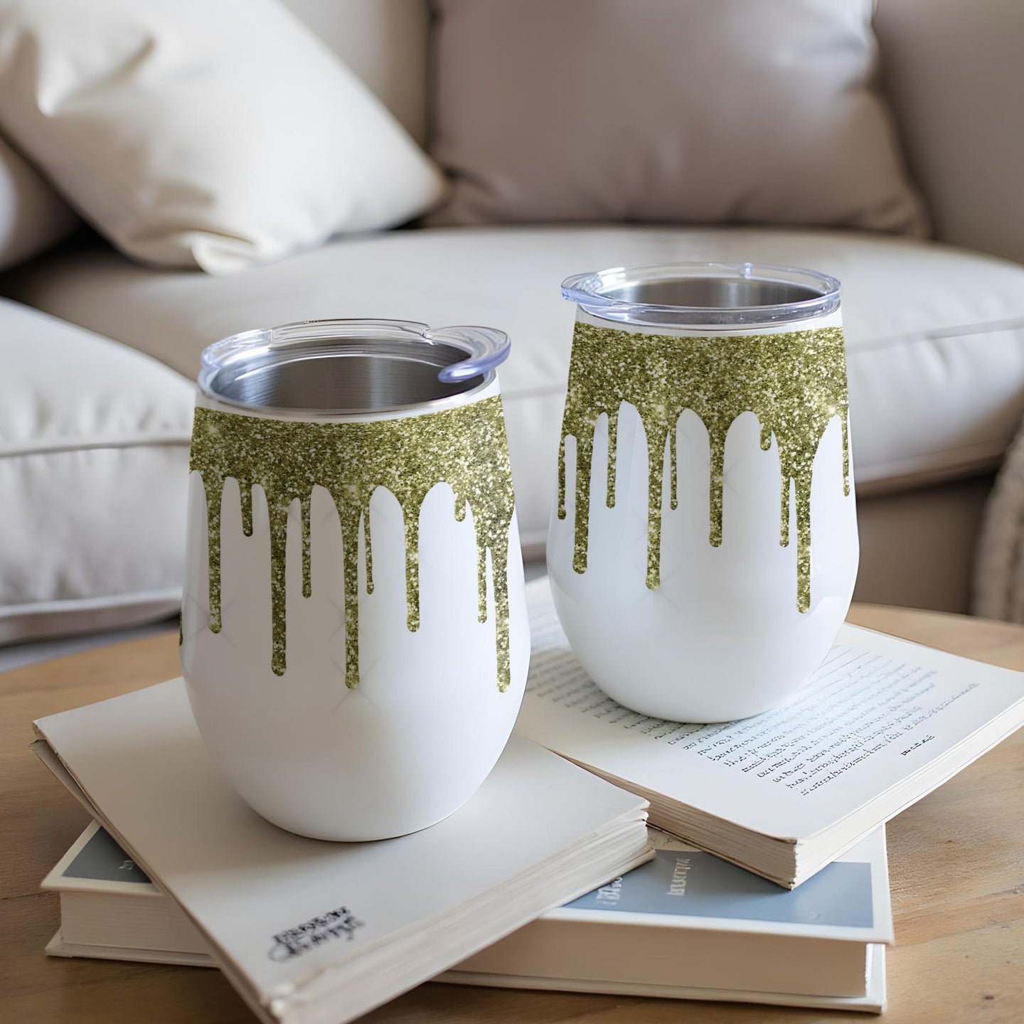 Two white tumblers with green glitter drip design, on books.