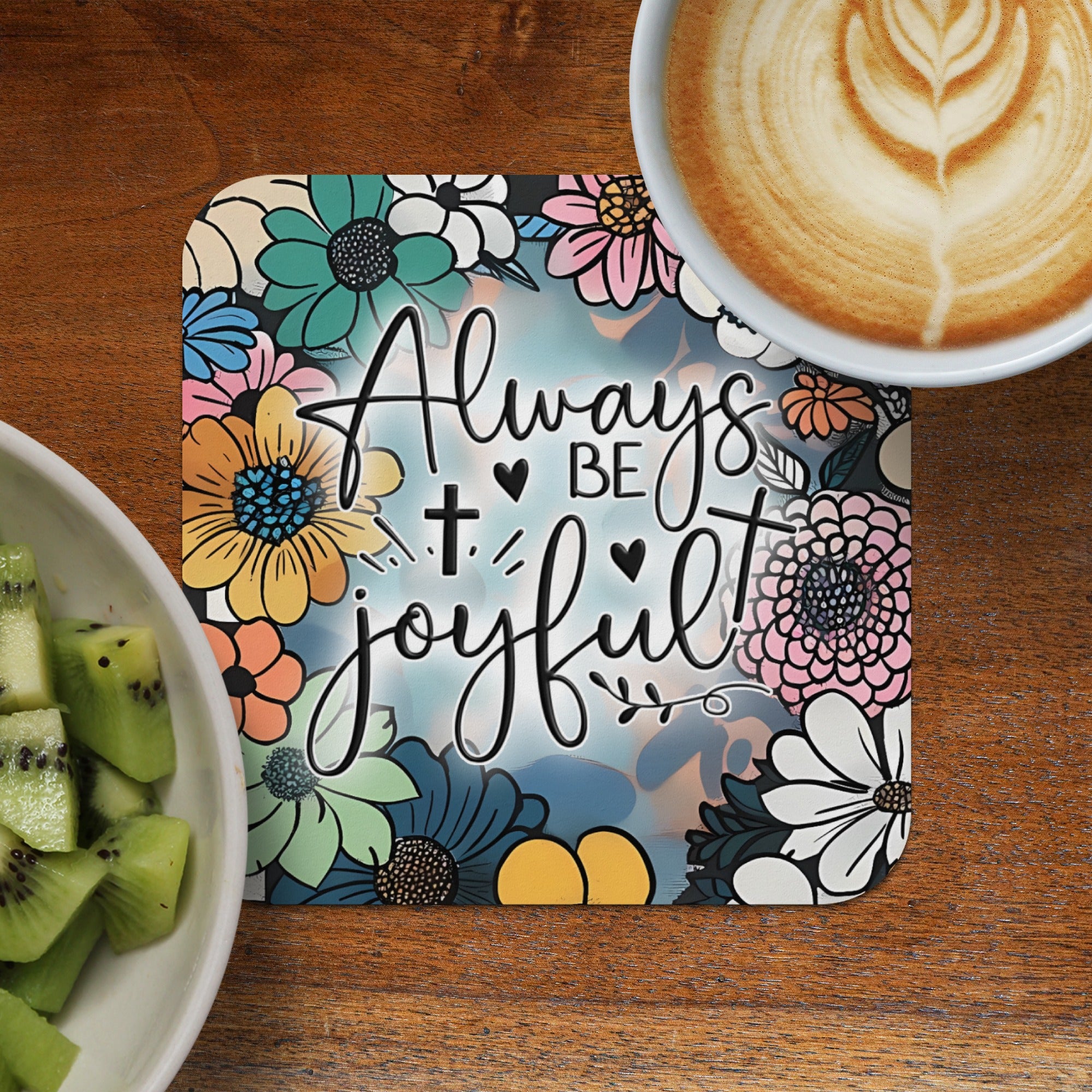 Coaster with "Always be joyful" text and floral border next to coffee and kiwi.