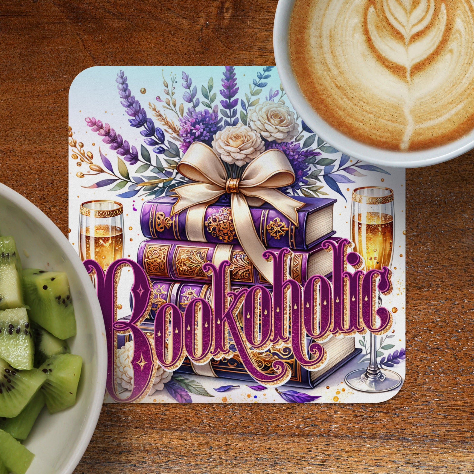 Stack of books with "Bookaholic" written in ornate purple lettering, near coffee and kiwi.
