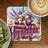 Stack of books with "Bookaholic" written in ornate purple lettering, near coffee and kiwi.