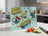 Cutting board with "Whisk Takers" and cartoon egg characters, with tomatoes and cucumber.
