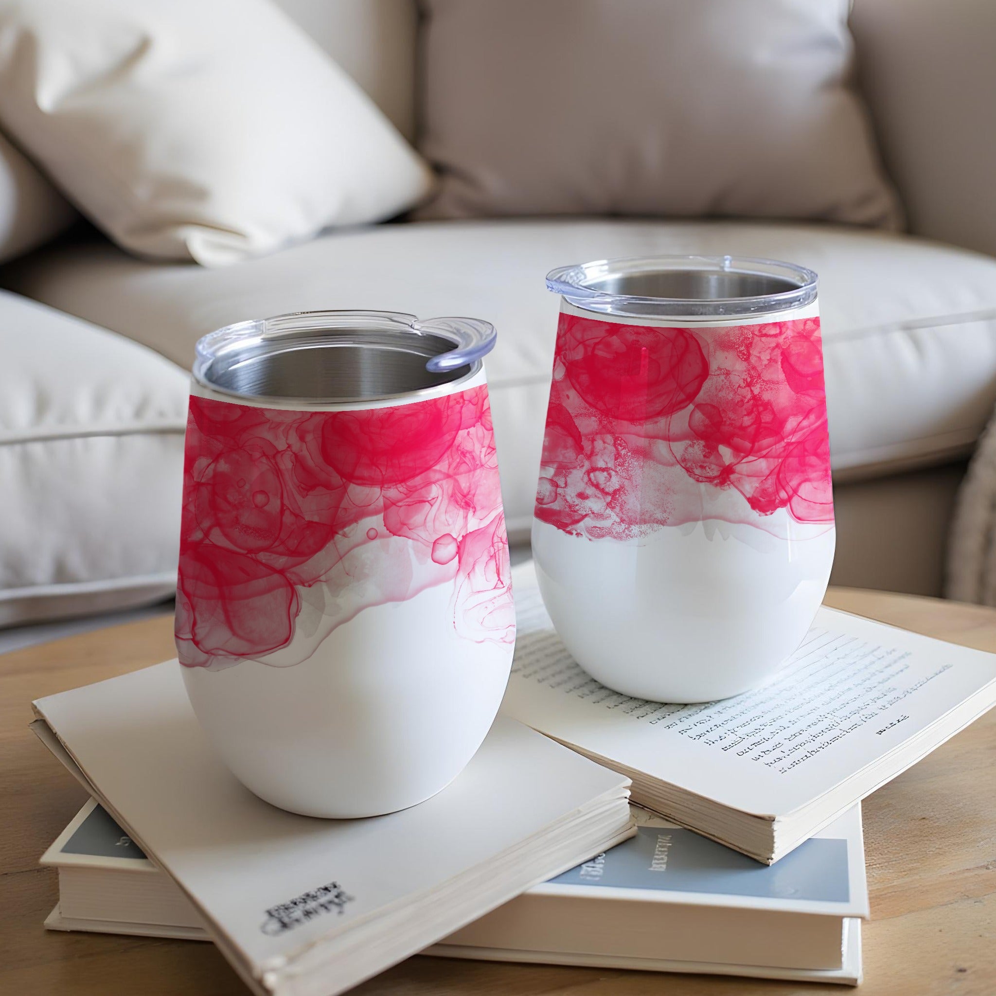 Two white wine tumblers with pink alcohol ink design on table.