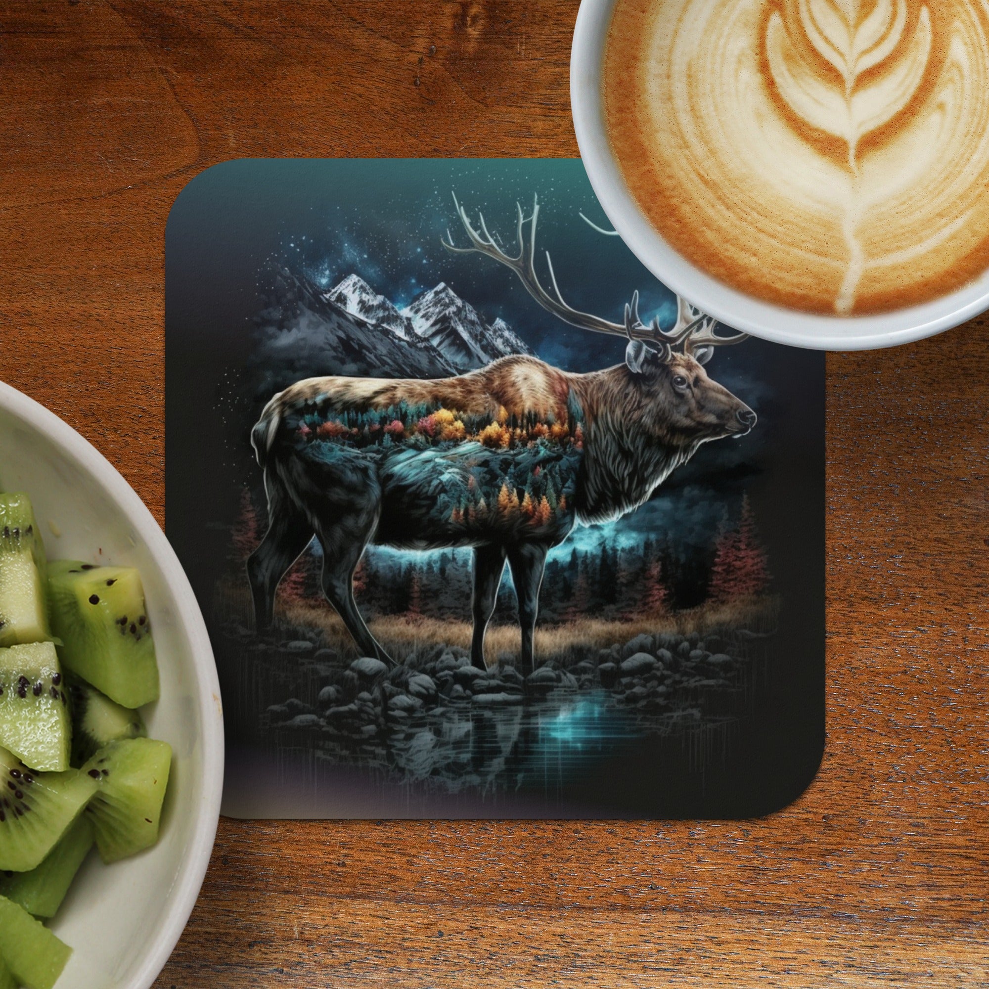 Elk with forest landscape overlay on a coaster next to coffee and kiwi.
