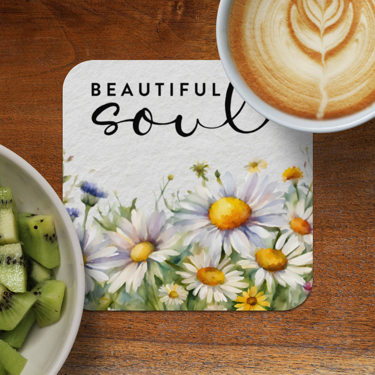 Coaster with daisies and "Beautiful Soul" text next to a kiwi fruit bowl and coffee.