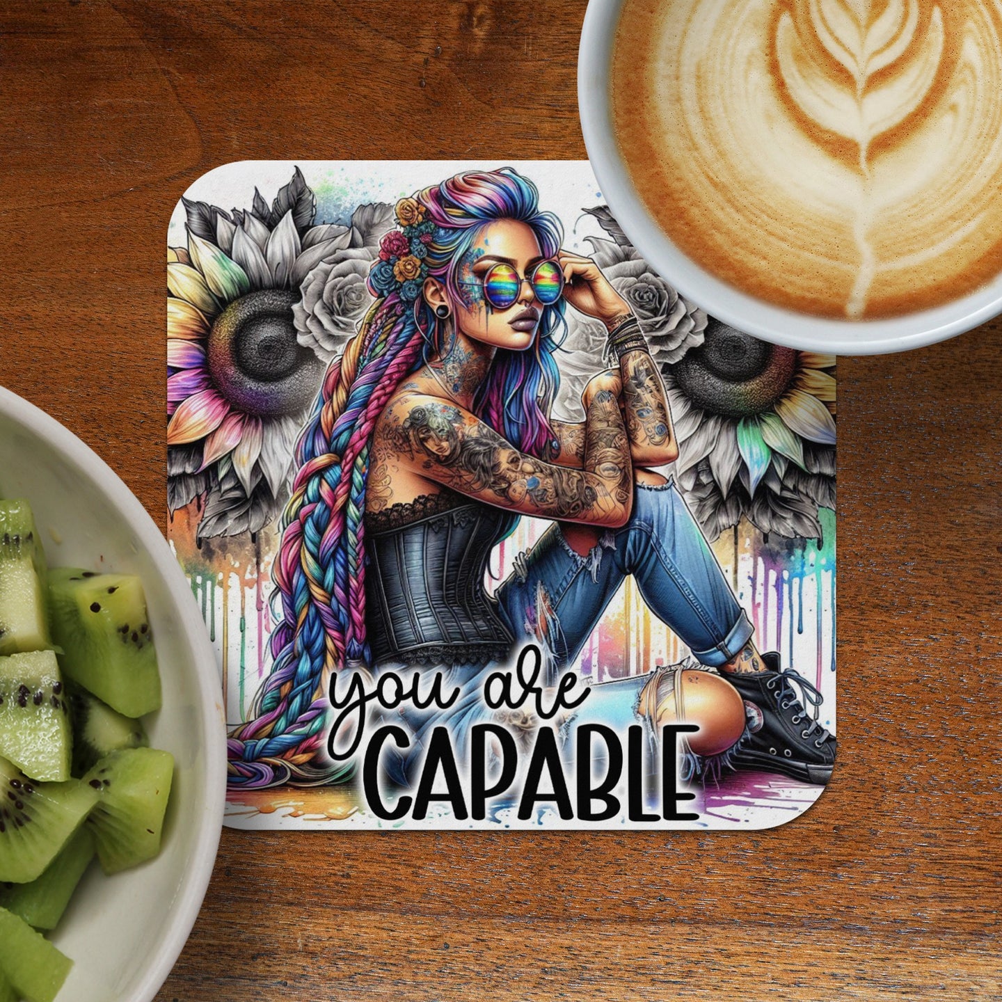 Woman with colorful braids and tattoos sits with sunflowers, text "you are CAPABLE".