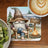 Gnome in cowboy hat sits by campfire with beer, near camper.