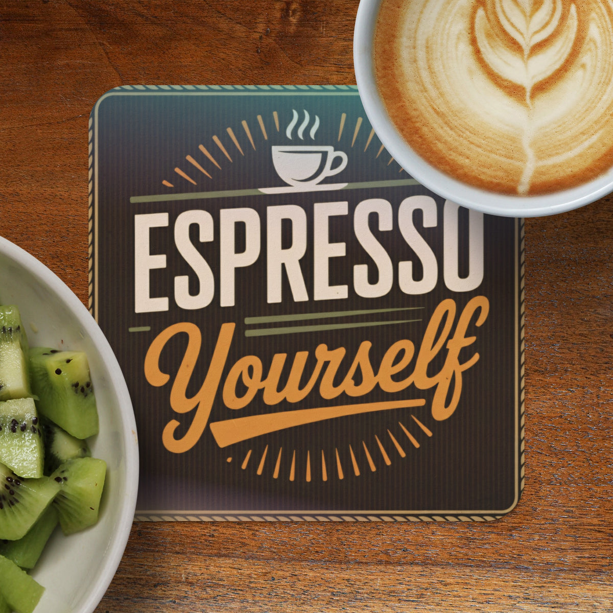 Espresso Yourself coffee coaster with latte art and sliced kiwi.