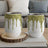 Two white tumblers with green glitter drip design and silver lids.