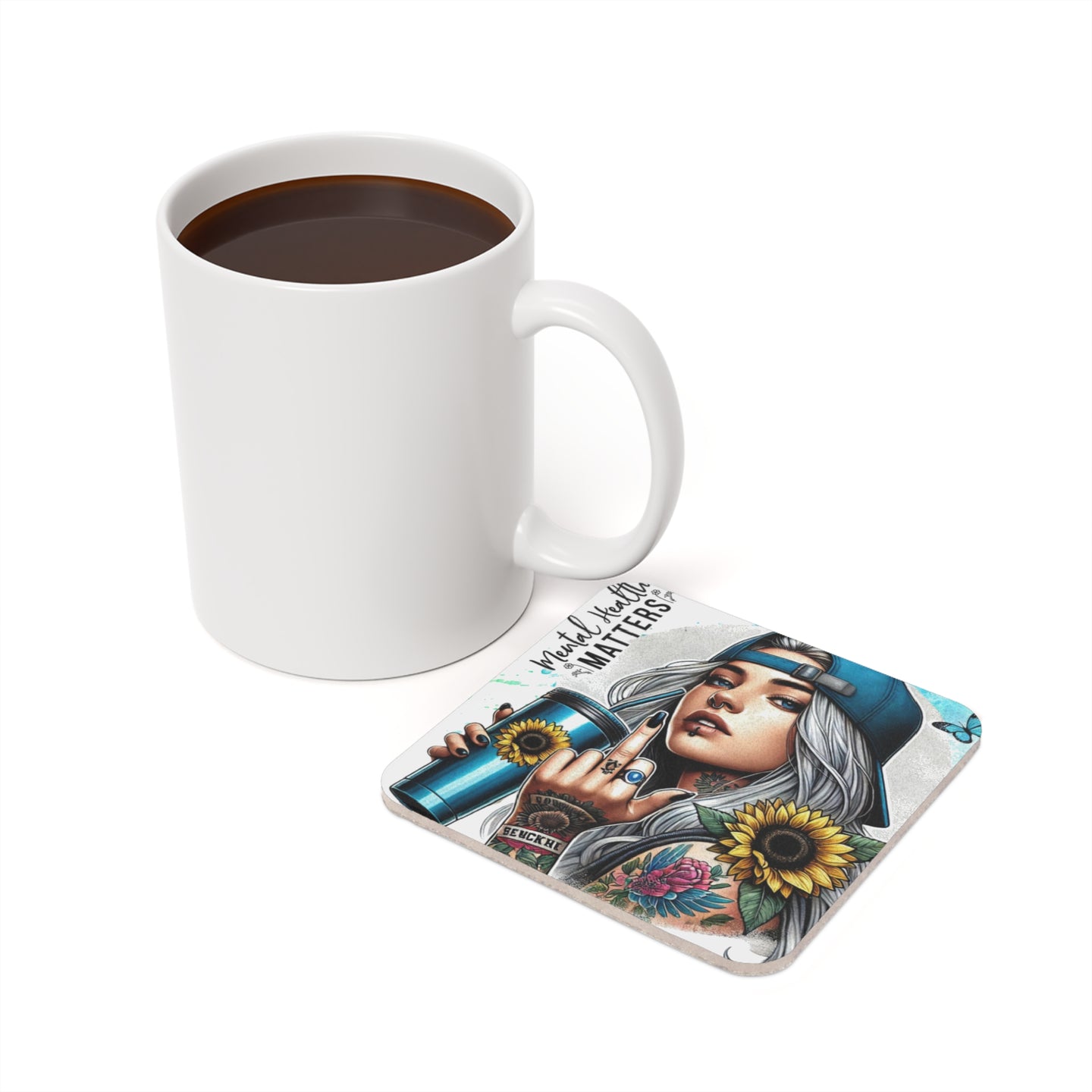 White mug beside a coaster with a tattooed woman, sunflowers, and text.