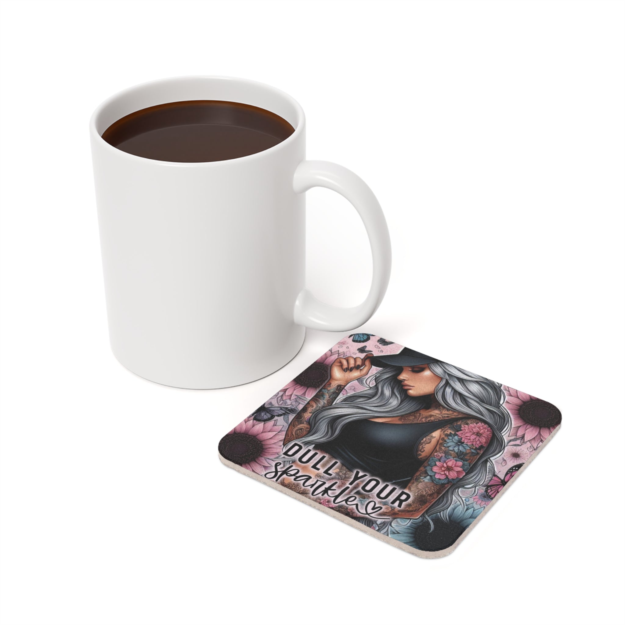 Mug of coffee next to square coaster with tattoo art and "Dull Your Sparkle" text.