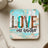 Square coaster with "LOVE one another" in patterned letters.