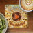 Coffee First Then Adulting coaster with play button, next to kiwi fruit and coffee.