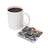 White mug and square coaster with colorful "Stay" tattoo art and flowers.