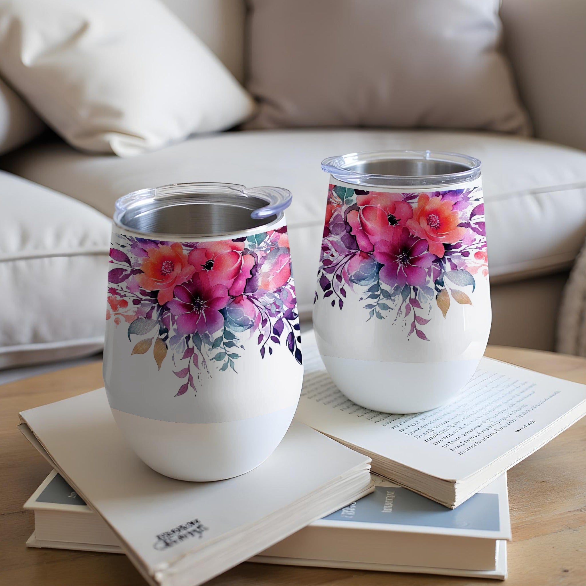 Two white tumblers with floral watercolor designs sit on books.