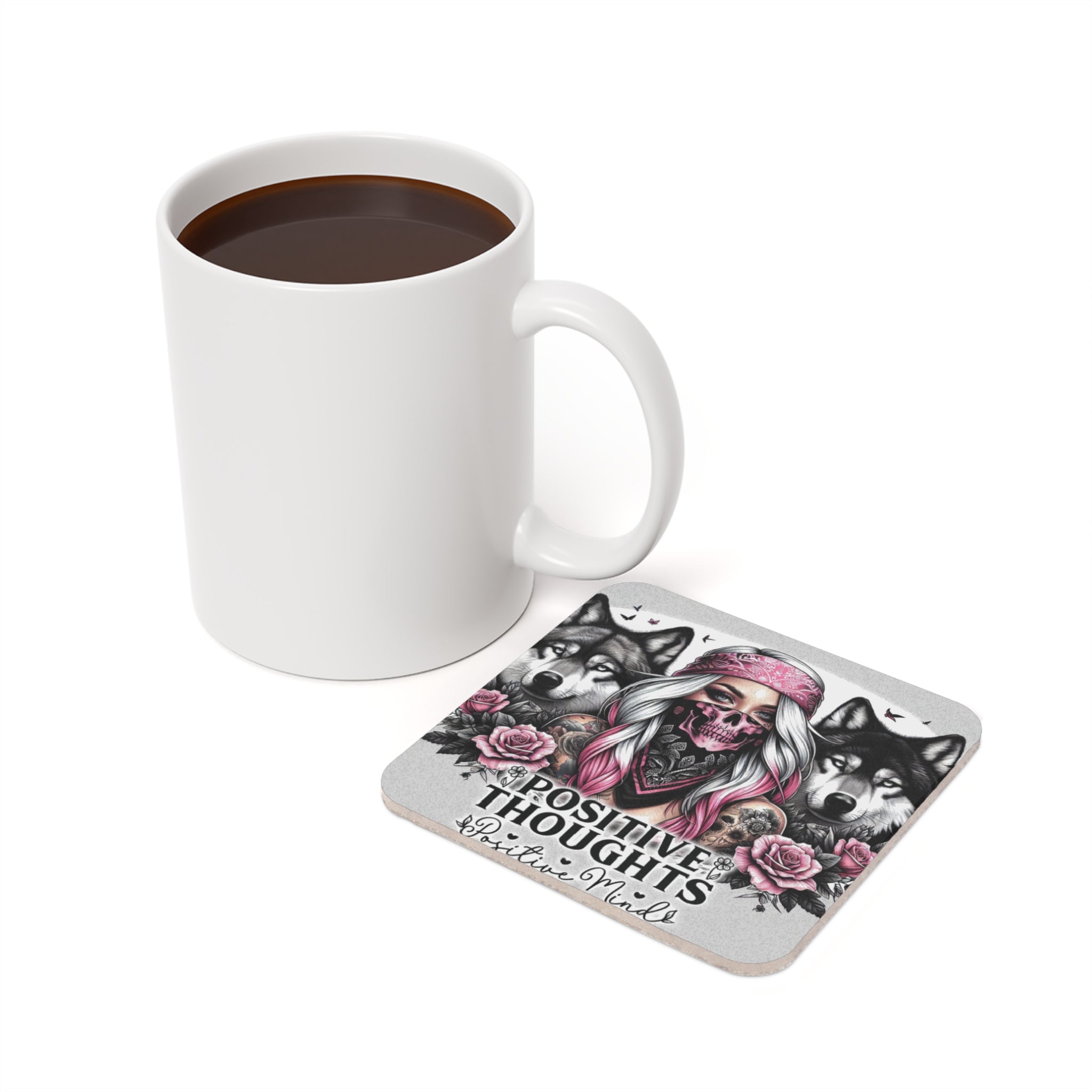 Mug of coffee next to a coaster with skull, roses, and wolves design.