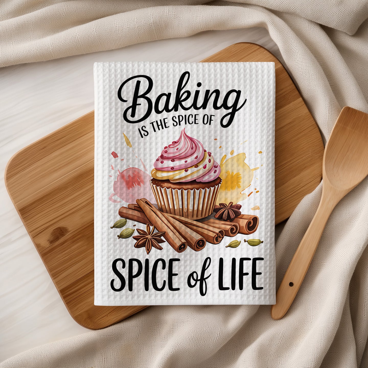 Towel with "Baking is the spice of life" text, cupcake, cinnamon sticks, and spices.