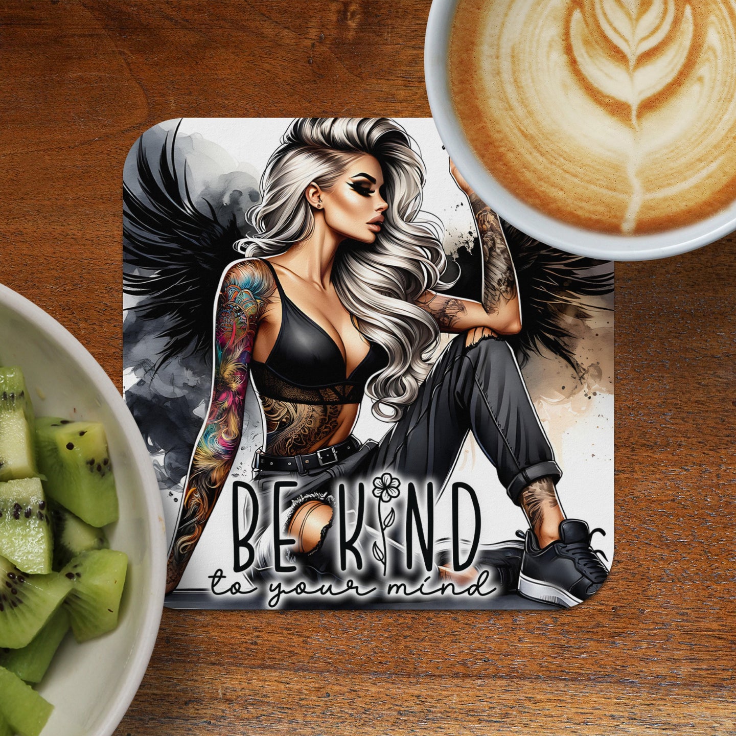 Tattooed woman with wings on coaster next to kiwi slices and coffee.