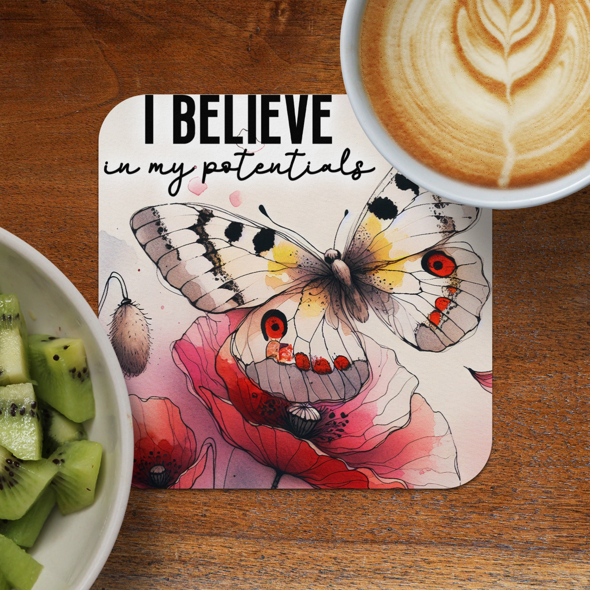 Coaster with butterfly and "I believe in my potentials" text, next to kiwi and coffee.