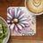 Coaster with purple and white daisy, ladybug, and "Create Change" text.