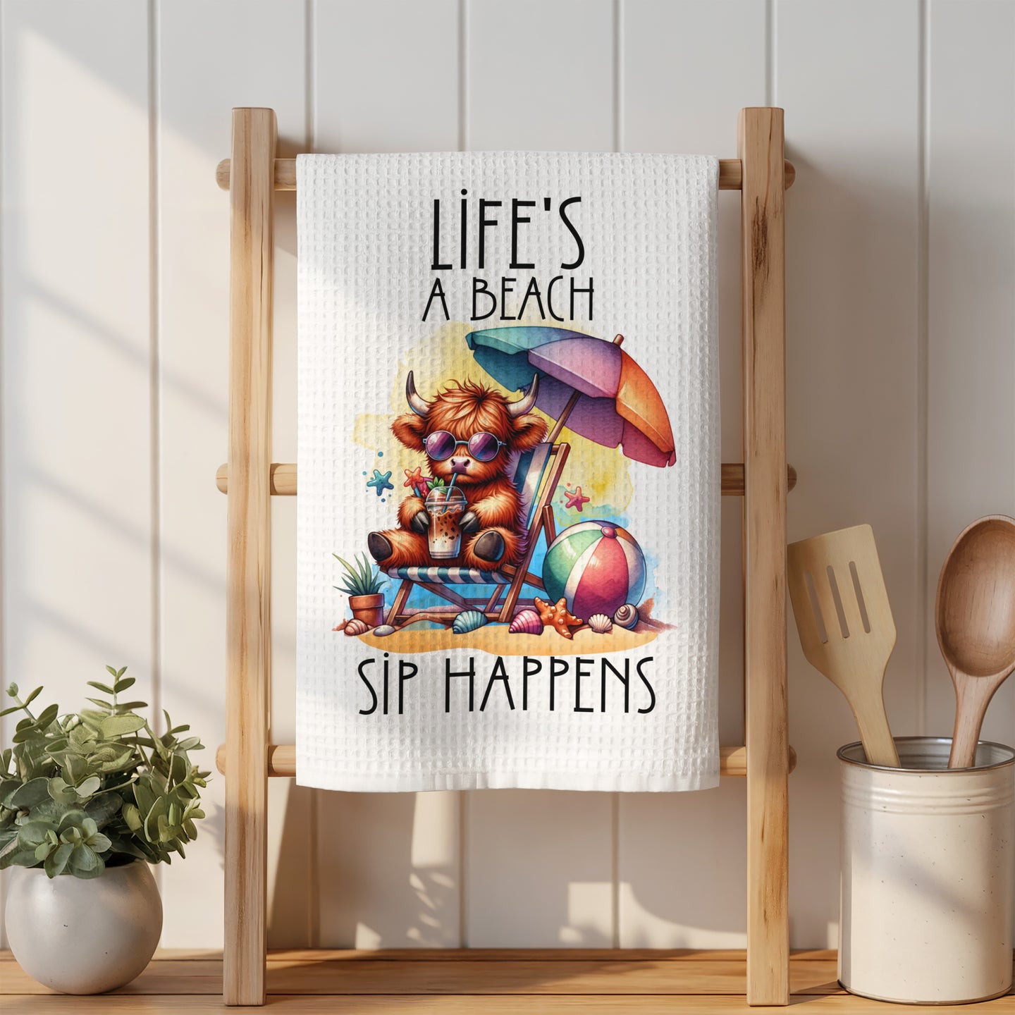 Towel with cartoon cow wearing sunglasses on beach with text "Life's a beach, sip happens".