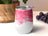 White tumbler with pink watercolor abstract design and purple grapes in background.