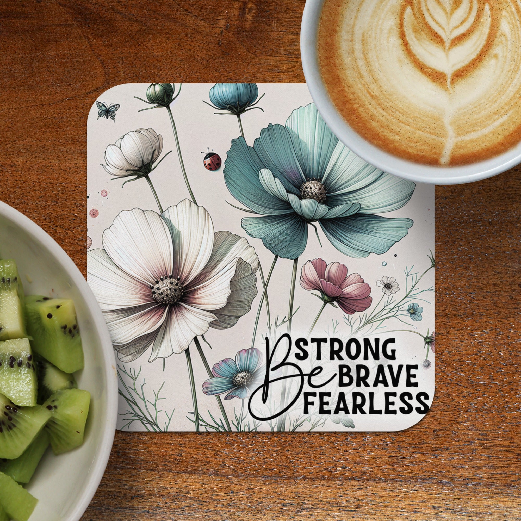 Coaster with flowers and "Be Strong Brave Fearless" text, next to kiwi and coffee.