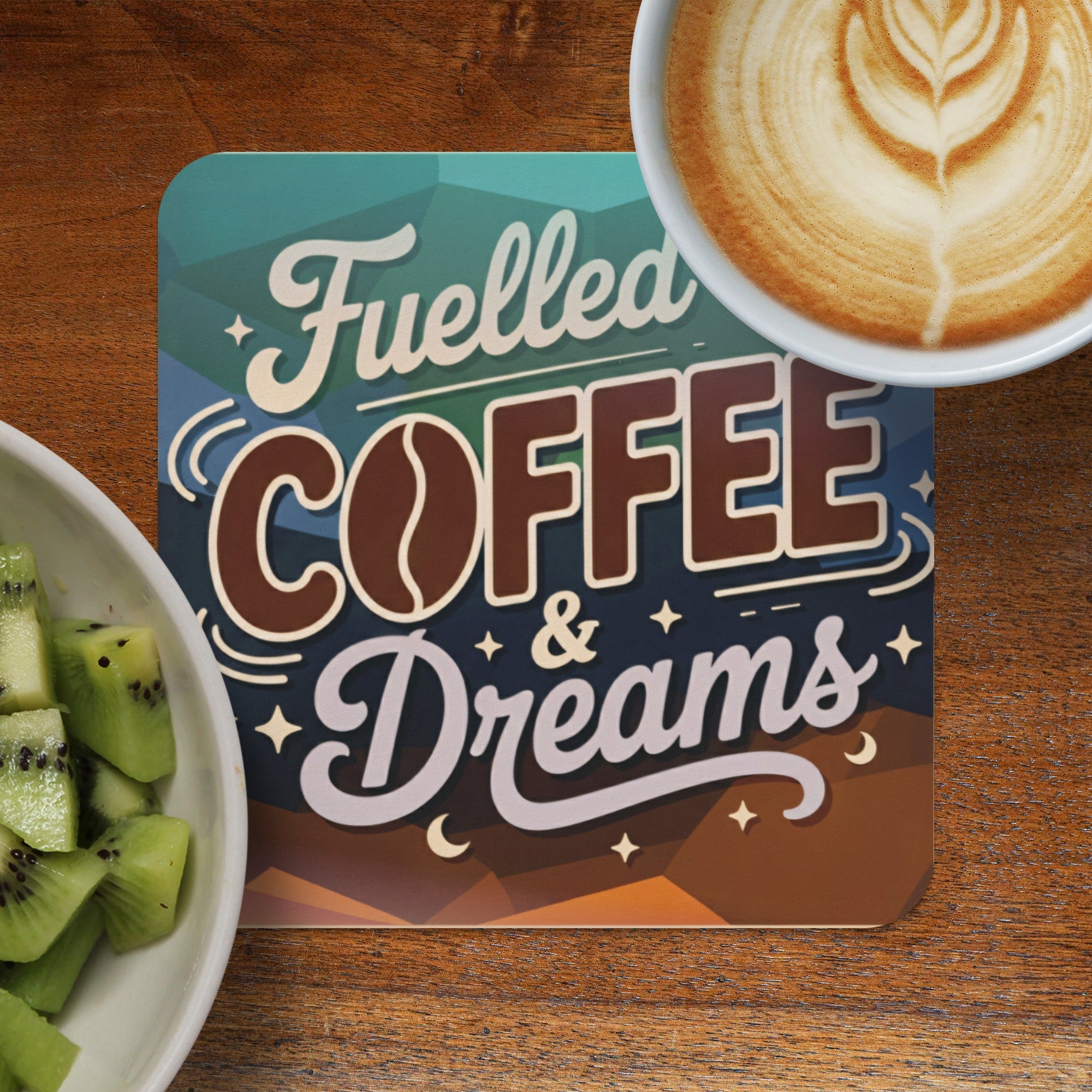 A coaster with "Fuelled COFFEE & Dreams" text next to a coffee and fruit bowl.