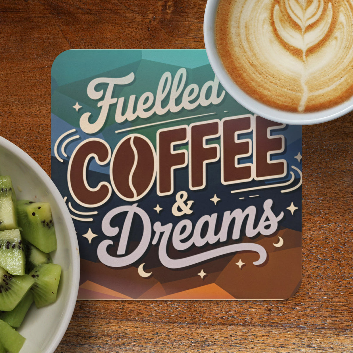 A coaster with "Fuelled COFFEE & Dreams" text next to a coffee and fruit bowl.