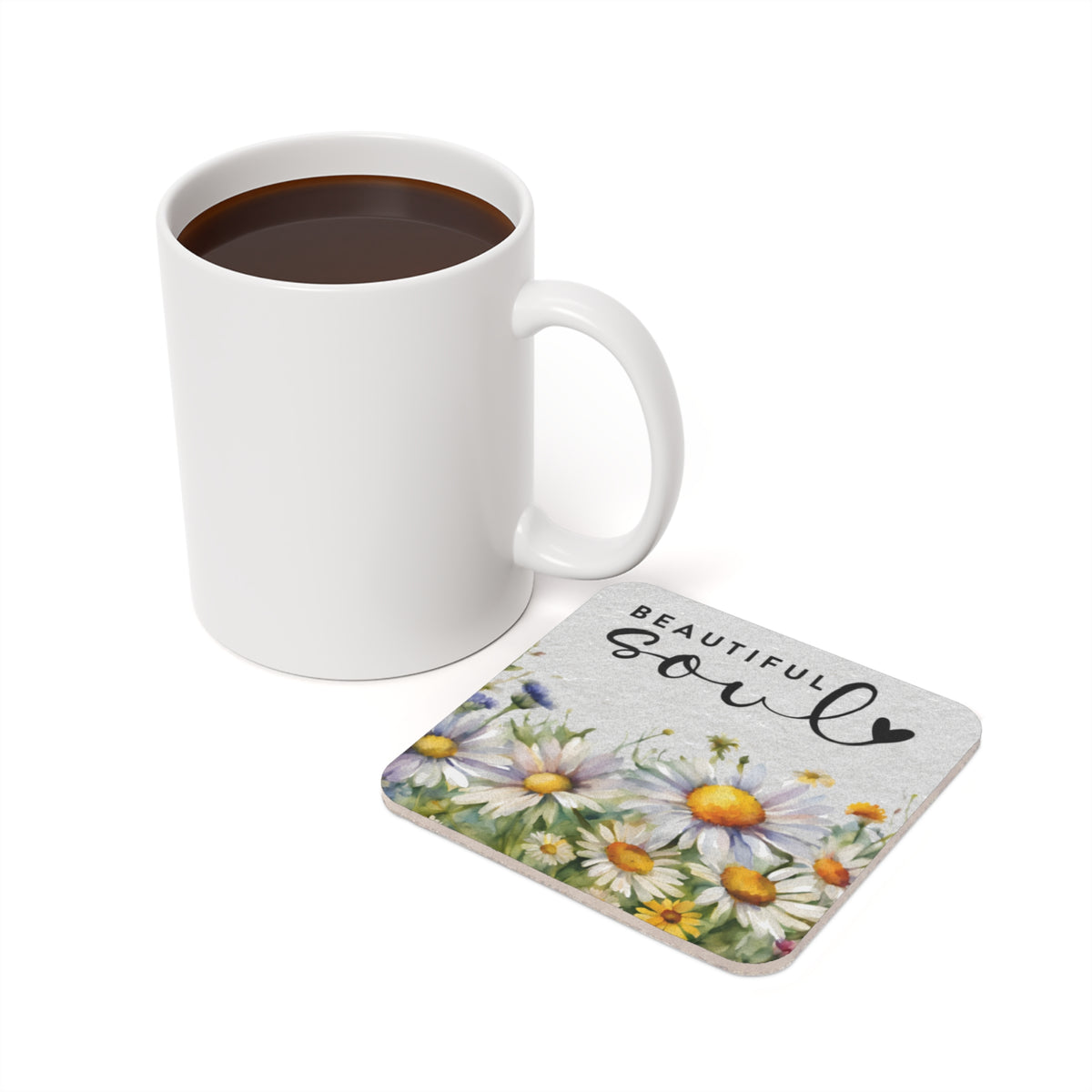 White mug of coffee next to a coaster with daisies and "BEAUTIFUL SOUL" text.