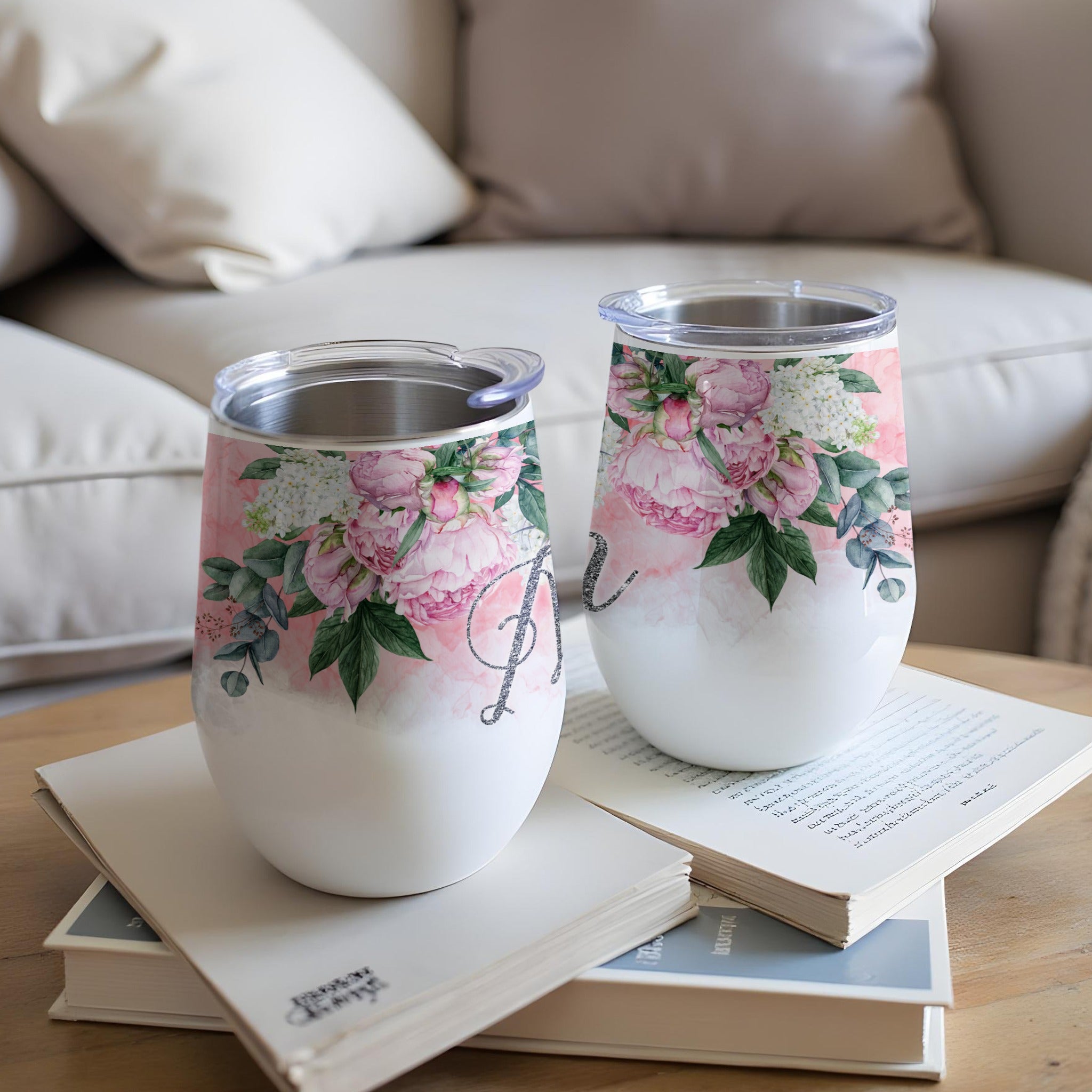 Two white stemless wine tumblers with pink floral designs and an initial "A".