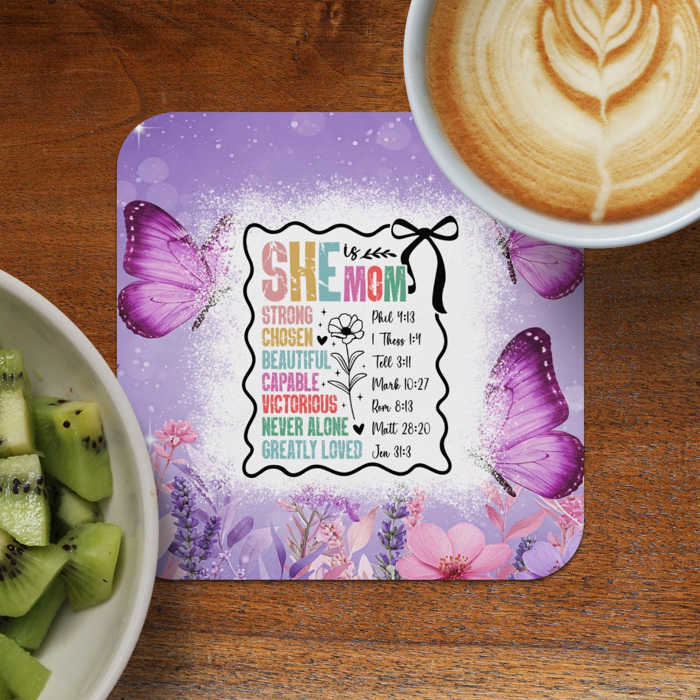 Coaster with "She Moms" text, Bible verses, and butterflies, next to kiwi slices.